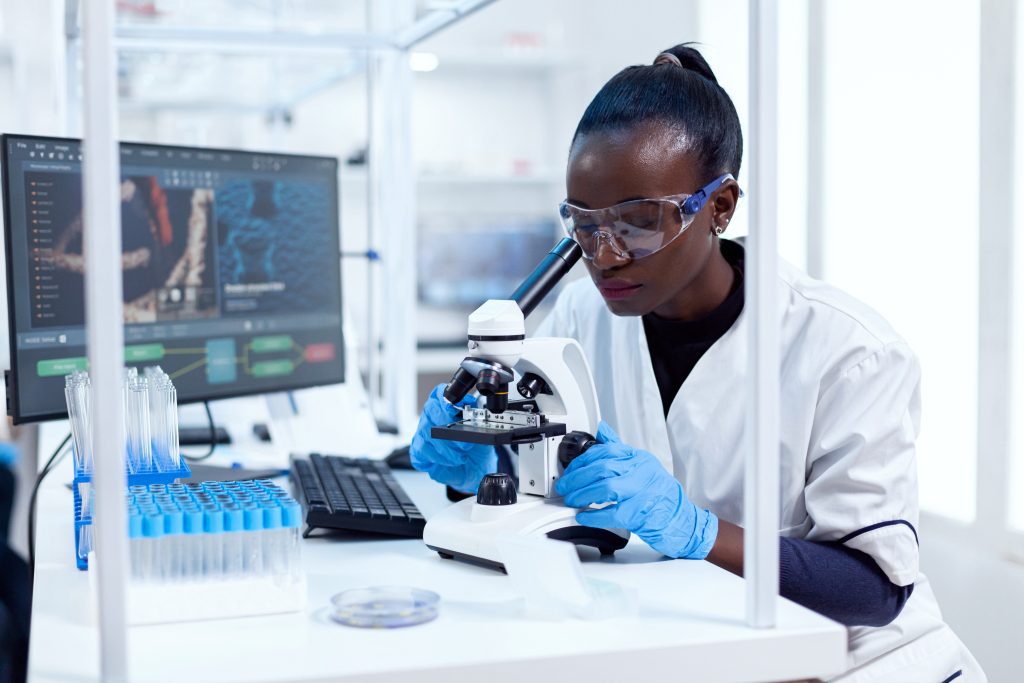 African,Researcher,Adjusting,Microscope,Lenses,Looking,At,Sample,On,Glass